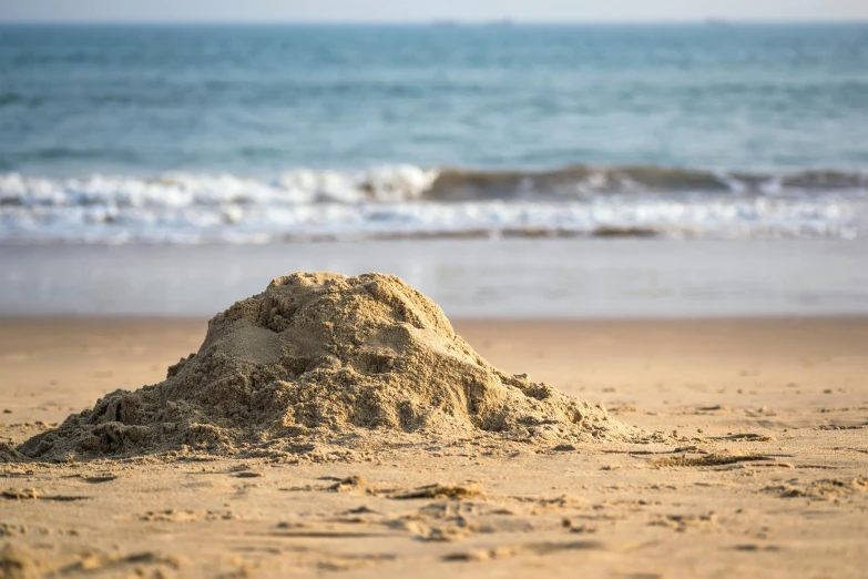 a pile of sand on top of a sandy beach near water