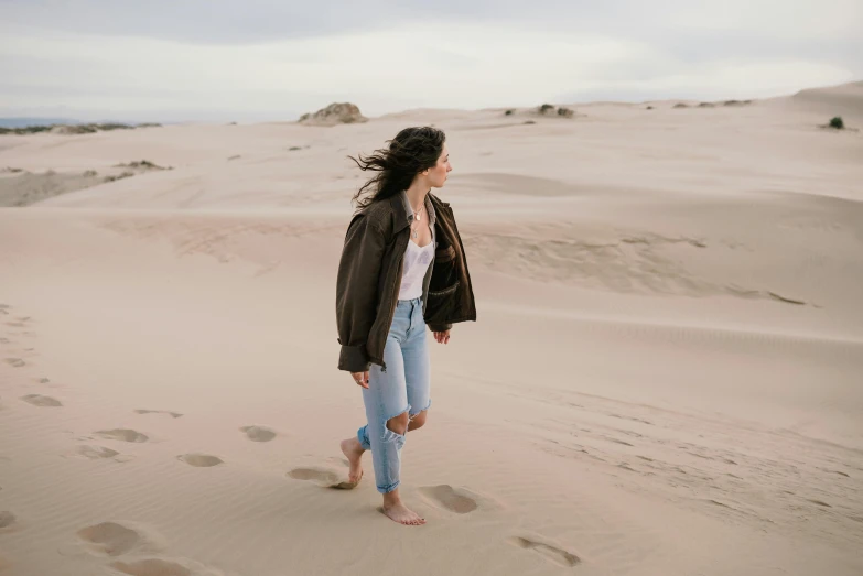 girl in jeans and jacket walking on a sandy field