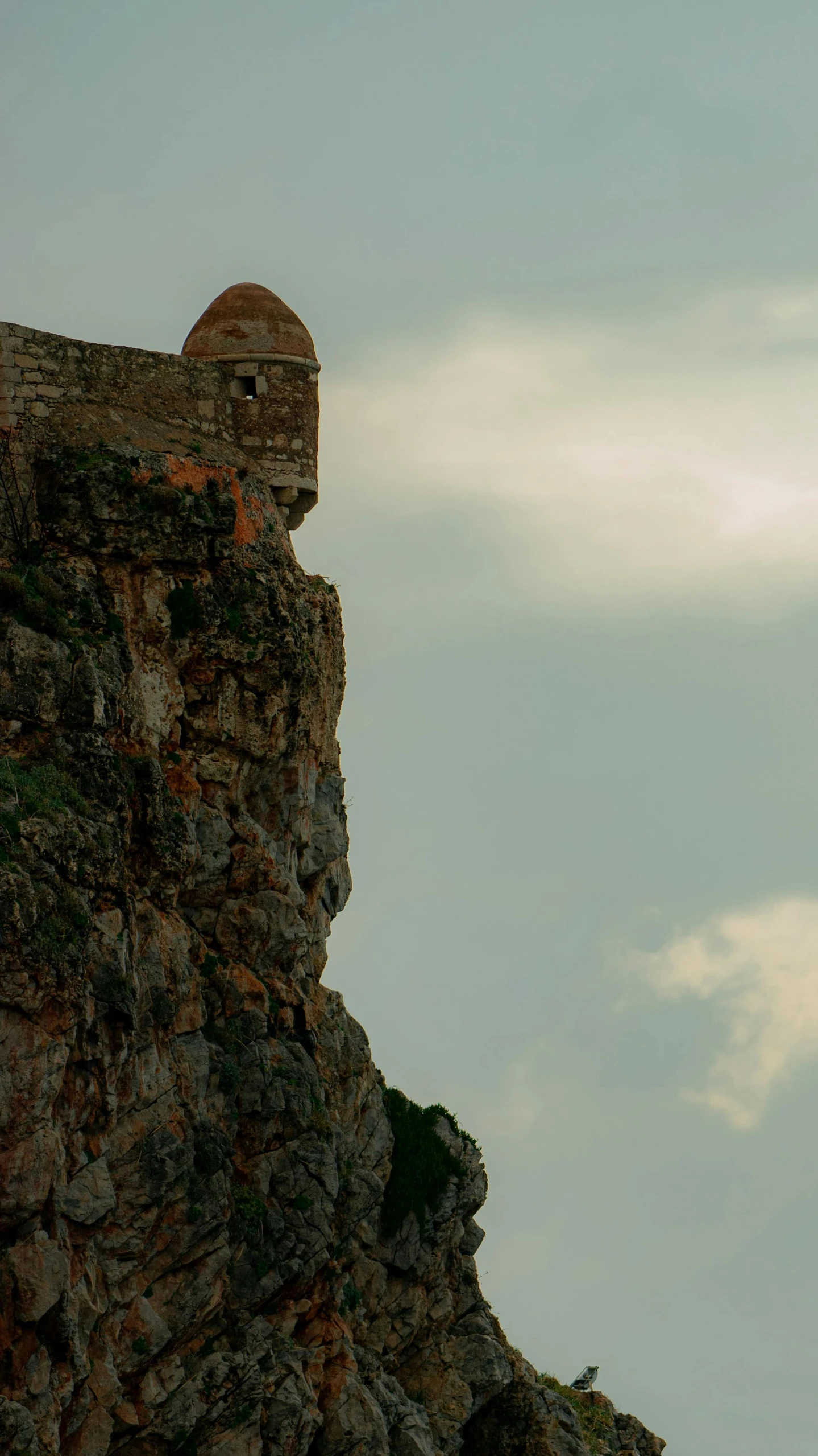 the lighthouse stands on a rocky cliff against a cloudy sky