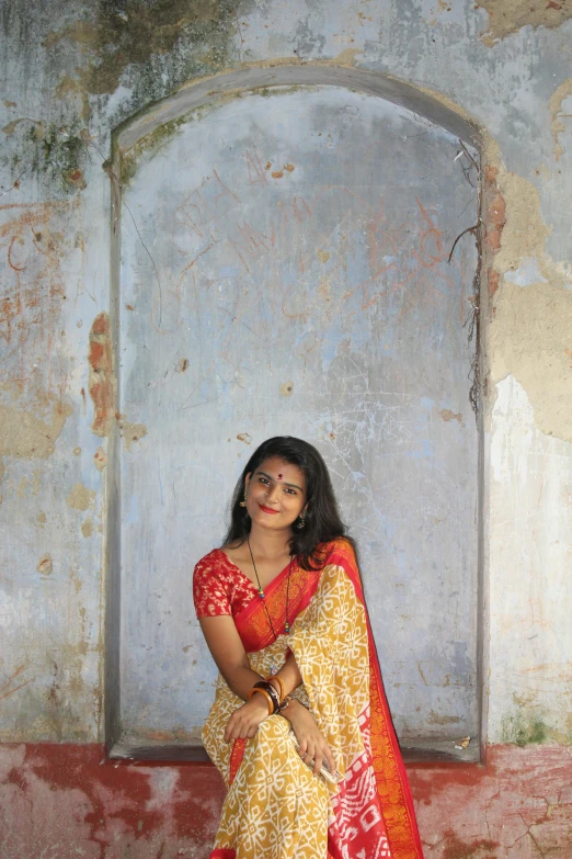 a woman wearing a red and yellow sari sitting in front of a window