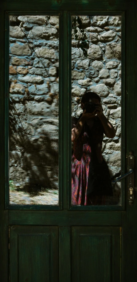 the woman is taking a po of herself through the glass of a green door