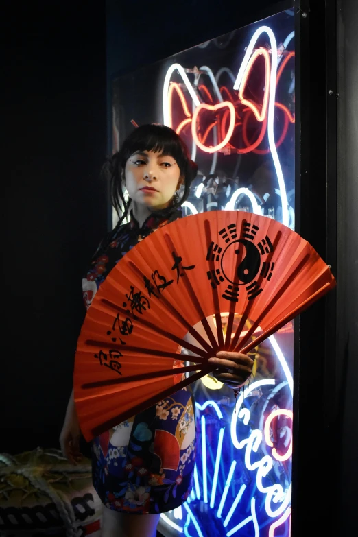 a person holding an orange fan next to a neon sign