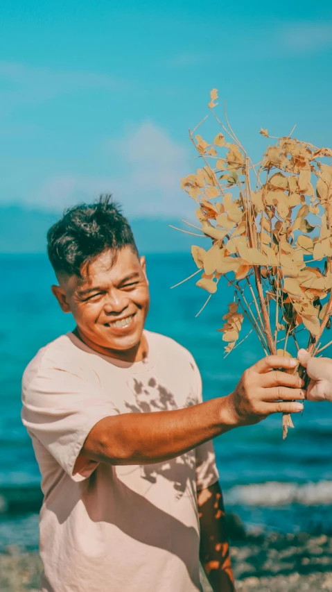 a man holding up dead leaves by the ocean