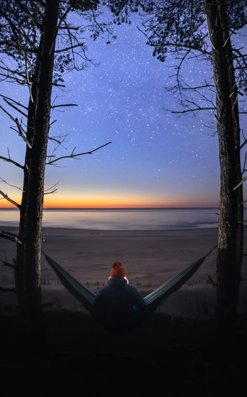 a person sitting in a hammock on top of a sandy beach under a starr filled sky