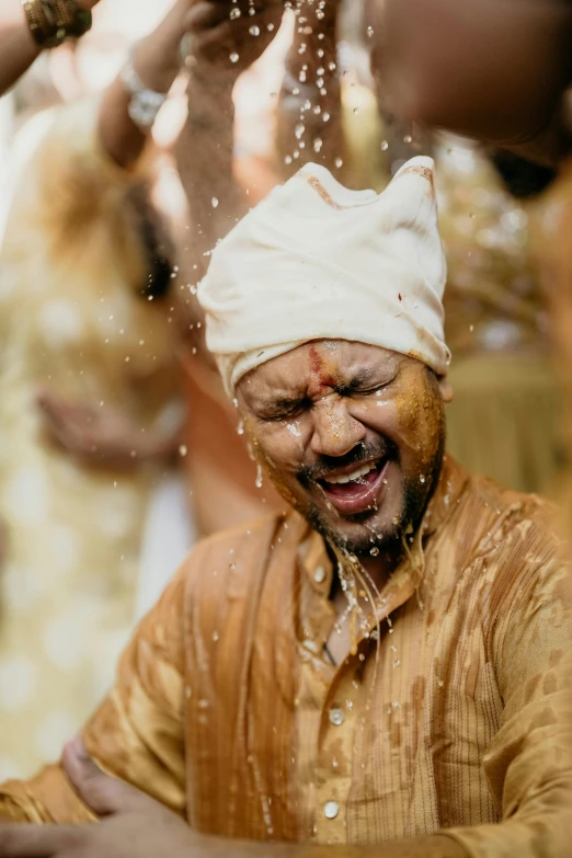 an indian groom with facial sprinkles pouring water over his face