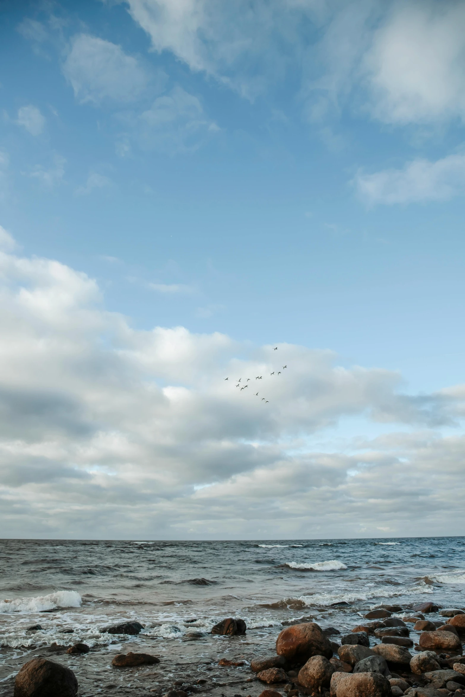 a beach with many rocks and birds flying in the sky