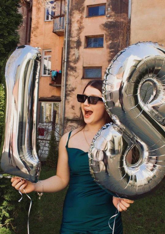 a girl holding up some silver balloons in front of a building