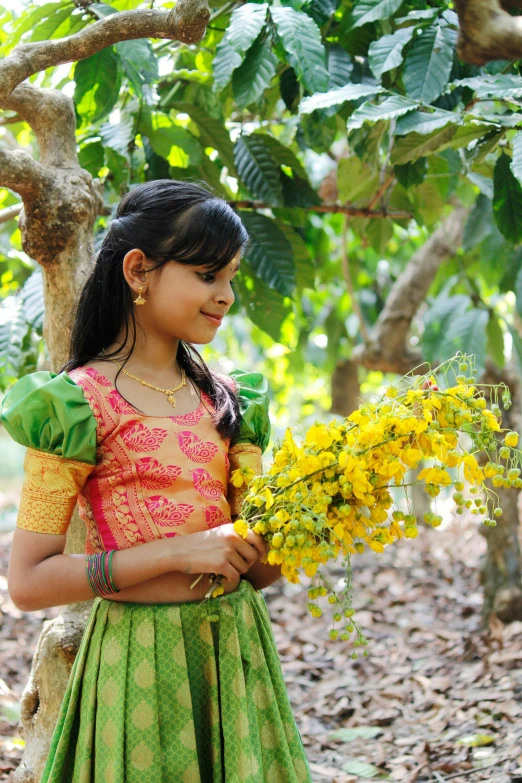 an indian woman wearing a green and yellow outfit holds flowers in her hands