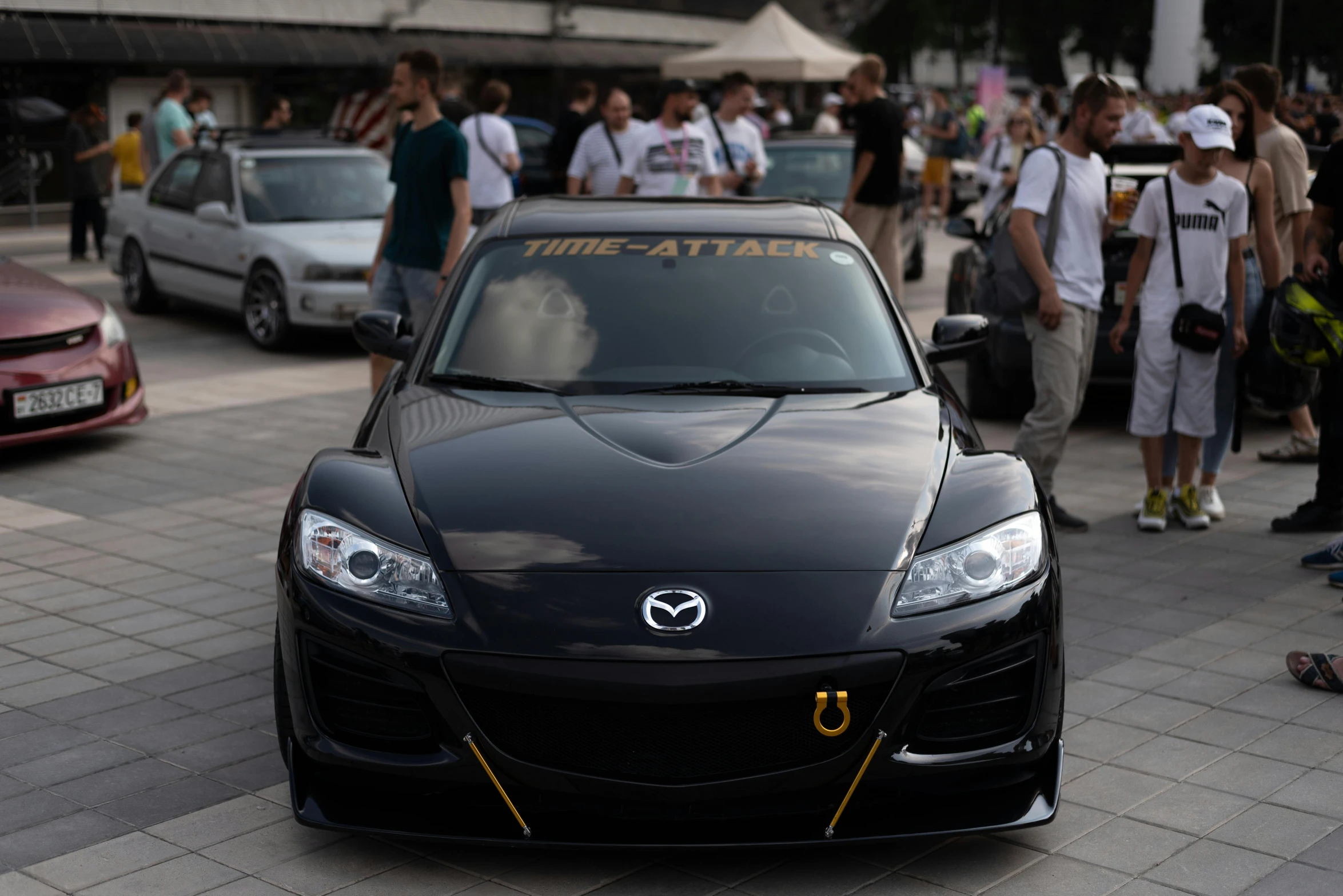 a black car with a yellow trim and a few people walking down a sidewalk in front of it