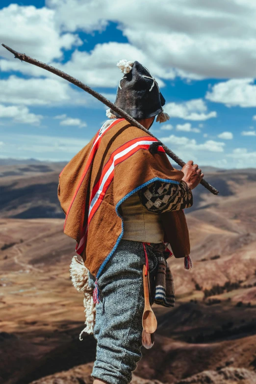 an indigenous man with long sticks and a brown outfit on