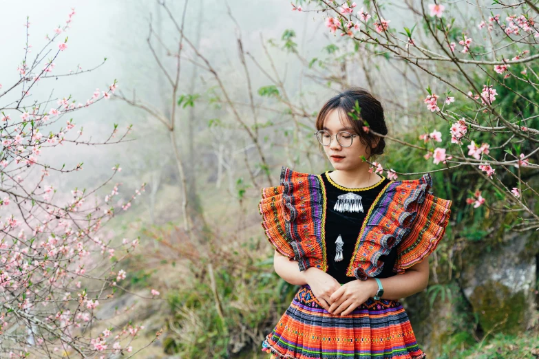 a  with glasses and dress standing in front of blooming nches