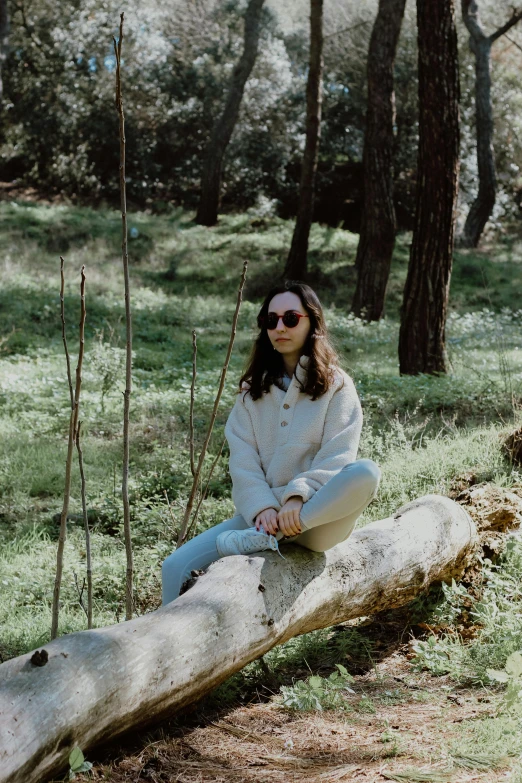 girl in white hoodie and jeans sitting on a log