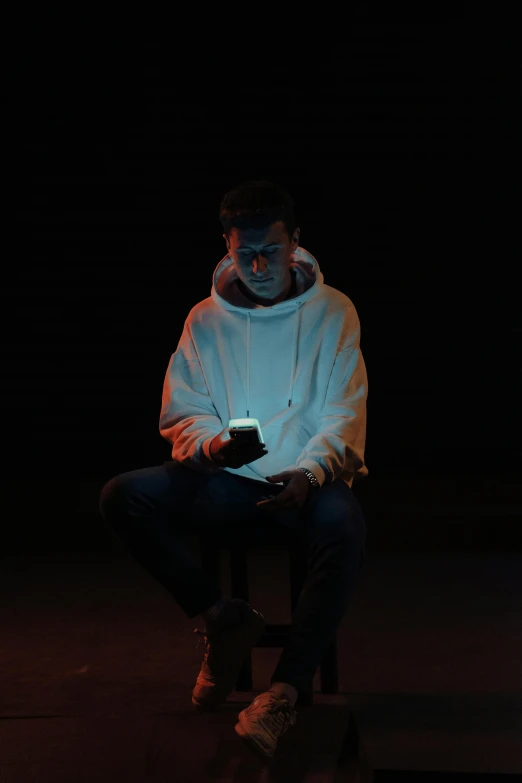 man seated on stool illuminated with cellphone