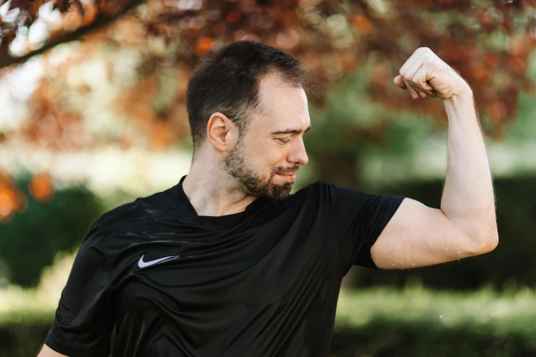 a man with a black shirt and a beard flexing his arm