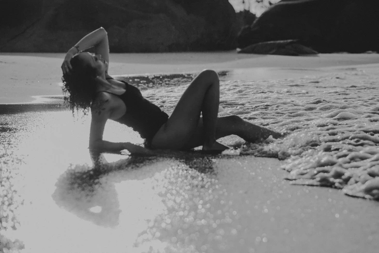 a black and white image of a woman lying on the beach