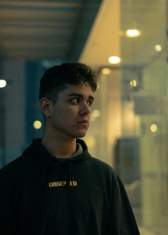 a boy stands in an airport terminal wearing a sweatshirt