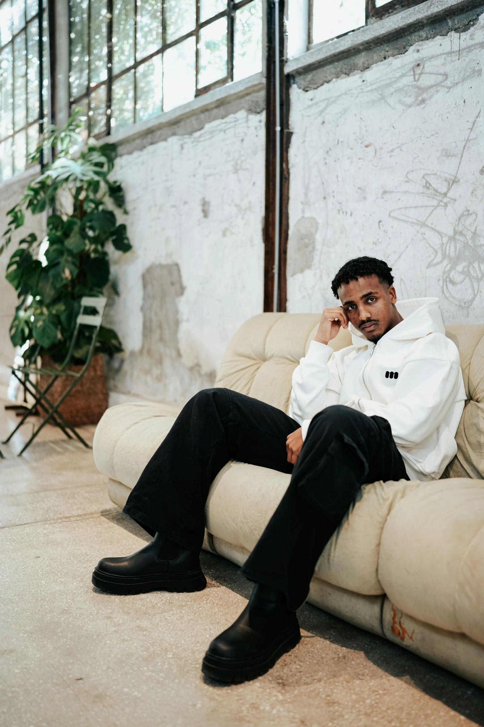 a man in white shirt sitting on couch next to a potted plant