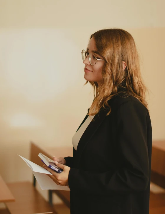 a woman standing in front of desks and holding papers