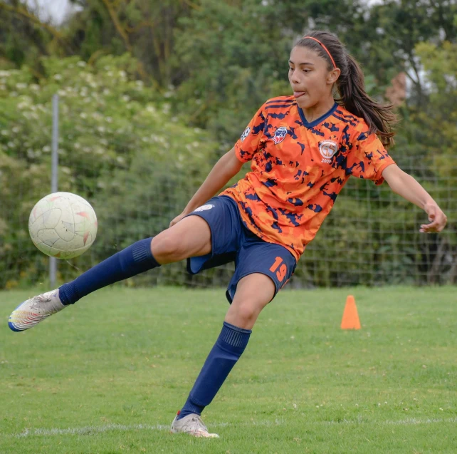 a woman kicking a soccer ball across a lush green field