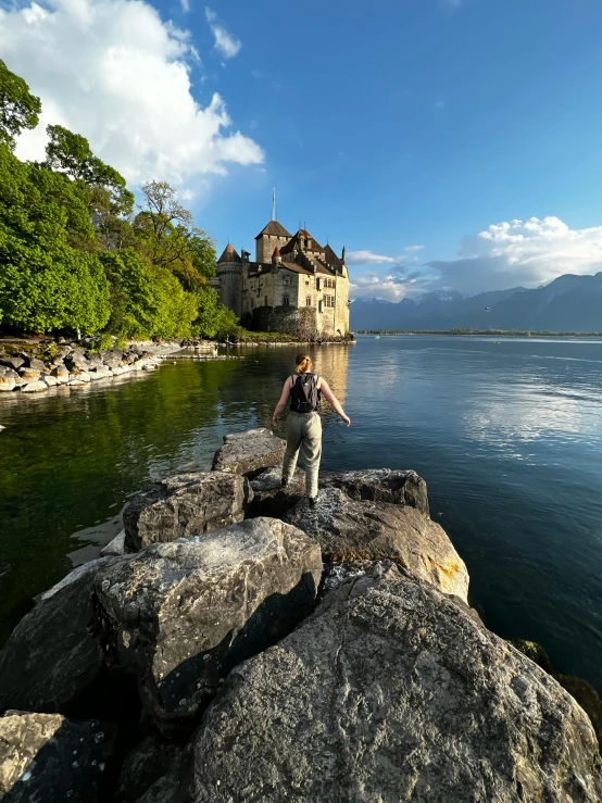 a man stands on rocks by the edge of the lake