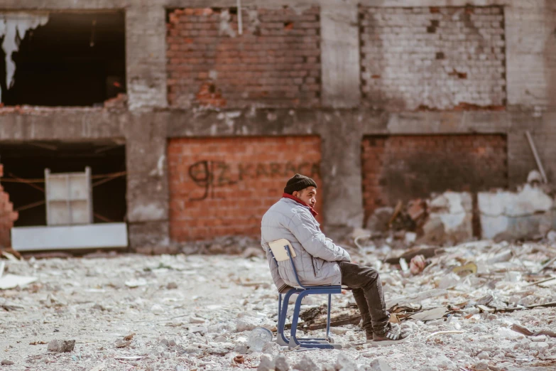 a man sitting in an old chair with a brick building behind him