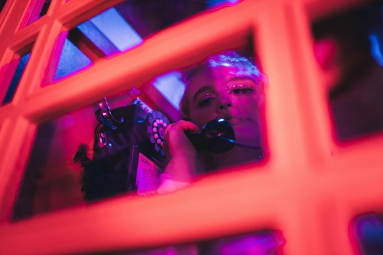 woman on phone looking through red mirror with window frame in background