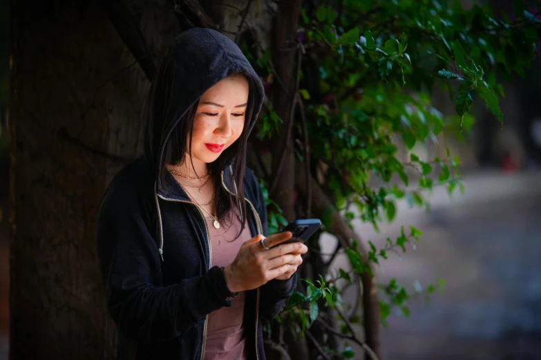 a young lady standing by a tree checking her phone