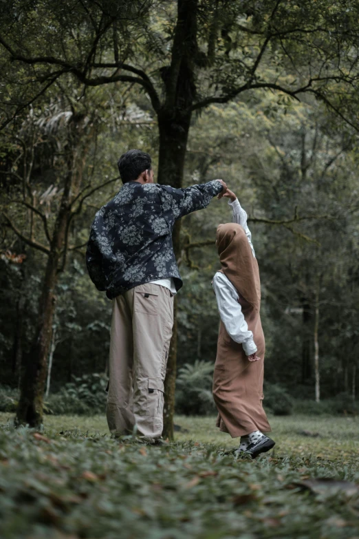 two people standing in the grass in front of trees