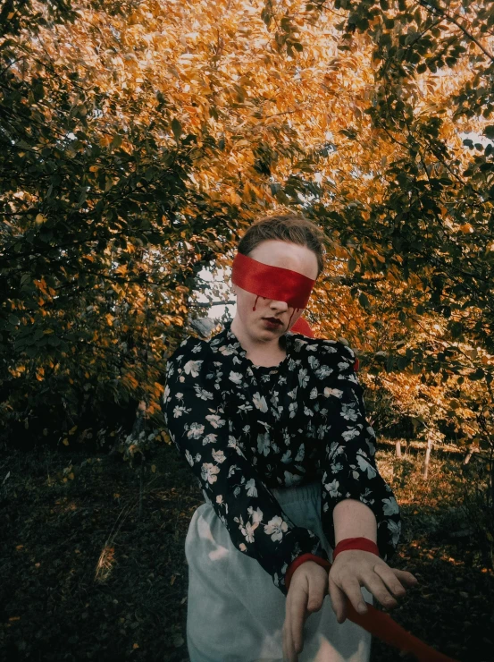 man with a blind on his face standing in front of trees