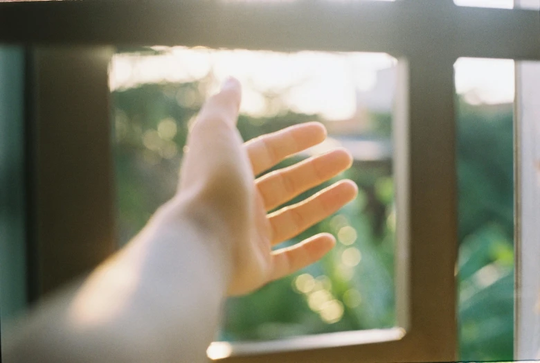 a hand reaches towards a small window to see soing outside