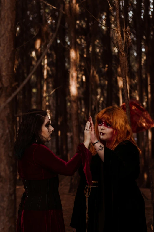 two women in black dresses standing in the woods with red hair