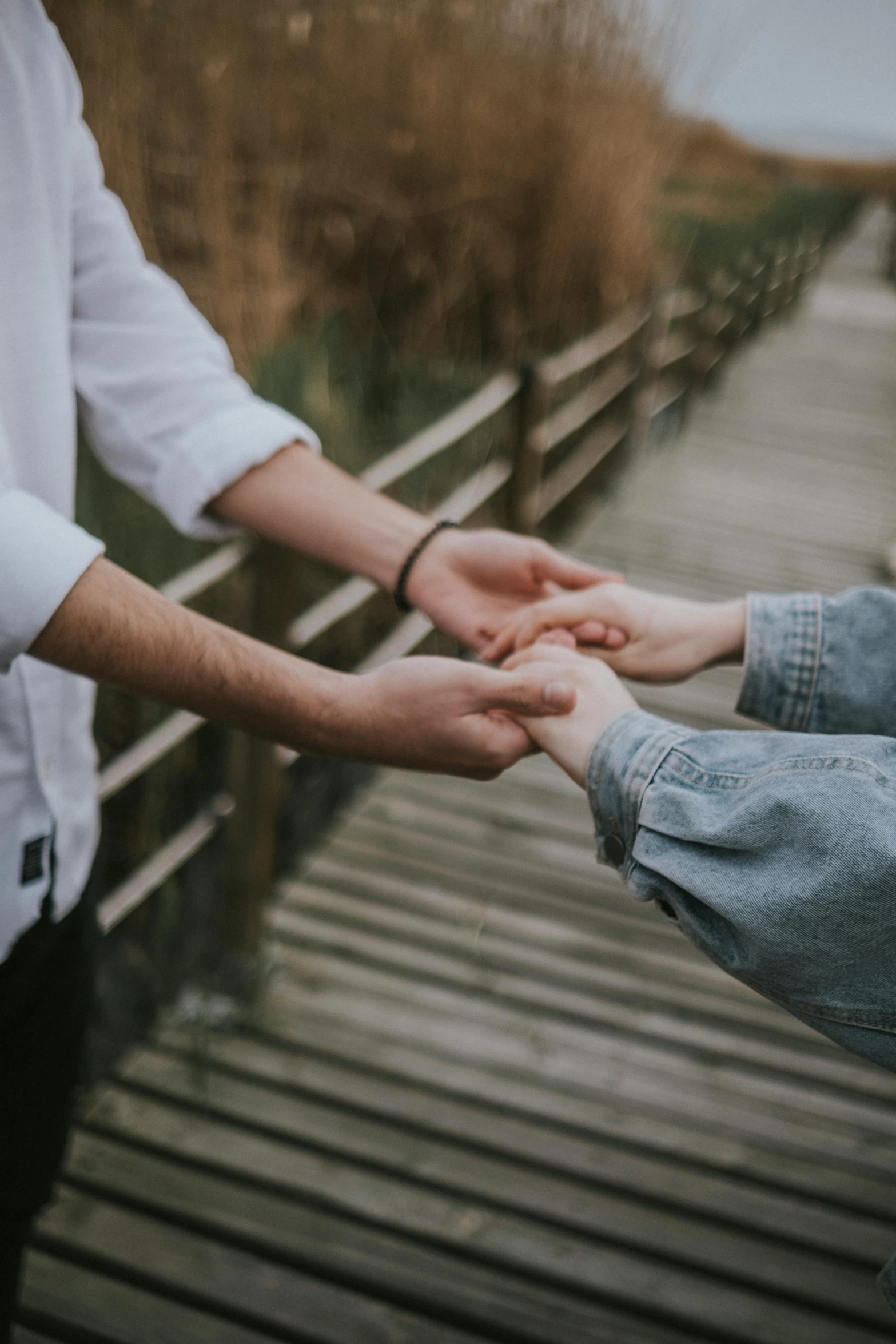 two people hold hands on a bridge over looking water