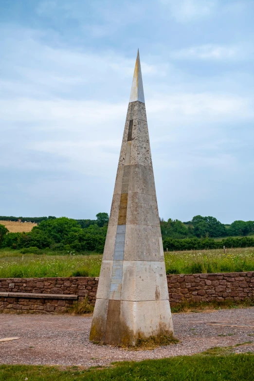 an obelisk in a park near a brick wall and trees