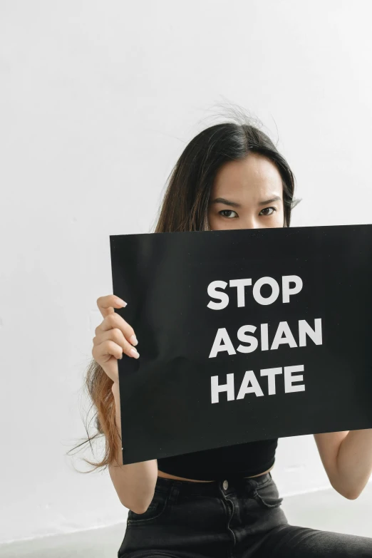 a woman holding a black sign reading stop asian hate