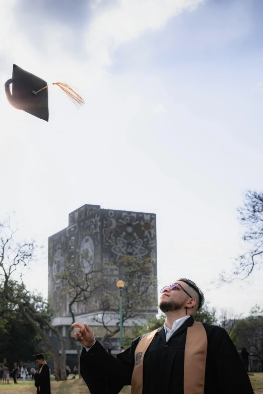 a man in graduation attire pointing at a light on top of a building