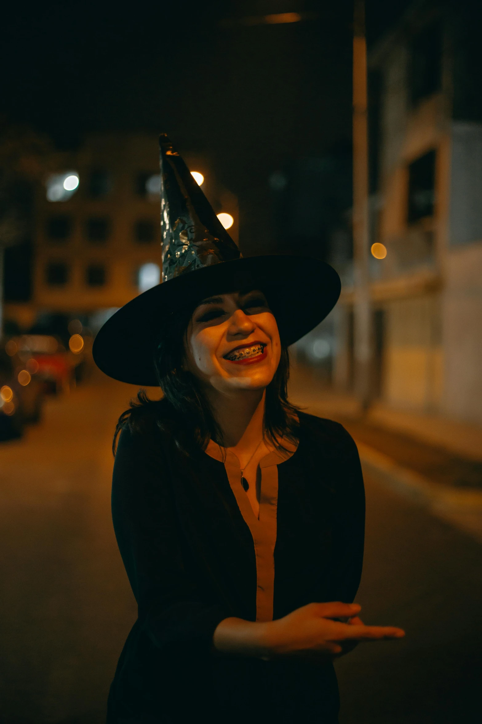 a woman wearing a witch's hat smiles while standing on the street