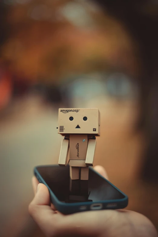 a tiny box man holding an iphone in his hand