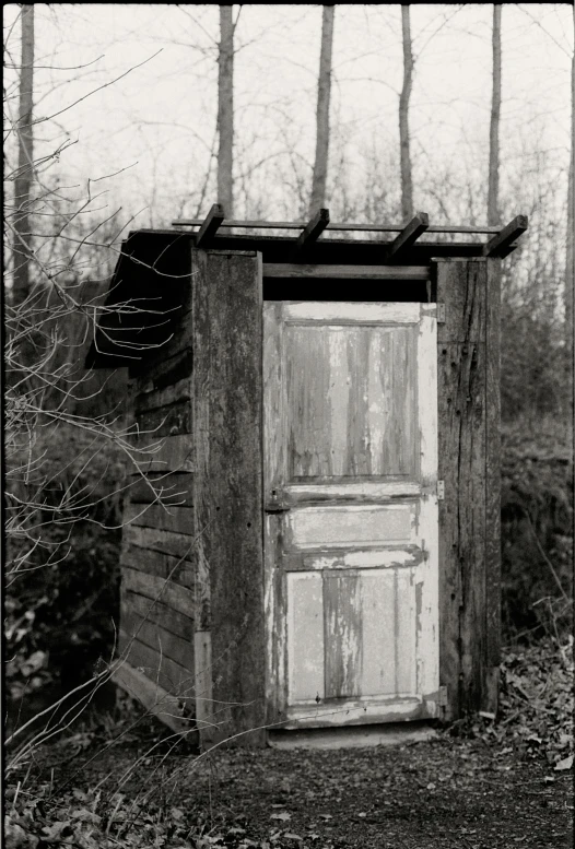 black and white image of an old outhouse in the woods