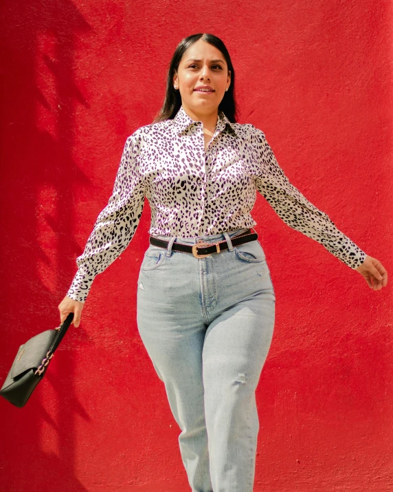 a woman in jeans and an animal print shirt is walking with a bat