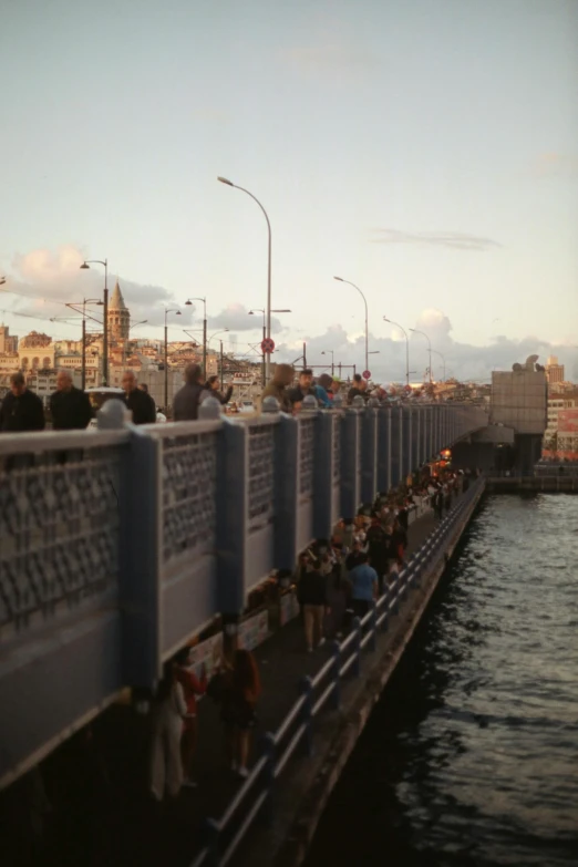 a long line of people walking along the sidewalk by water