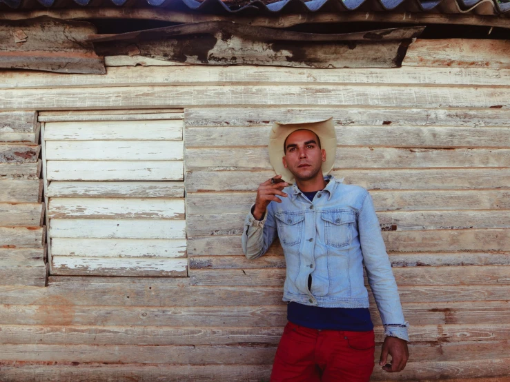 man with a hat on standing by an old wooden cabin