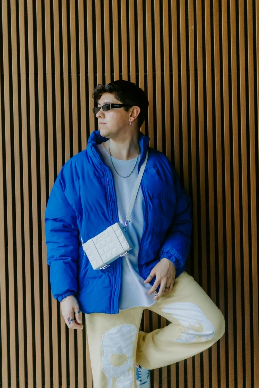 a man leaning against the wall in his blue jacket and jeans