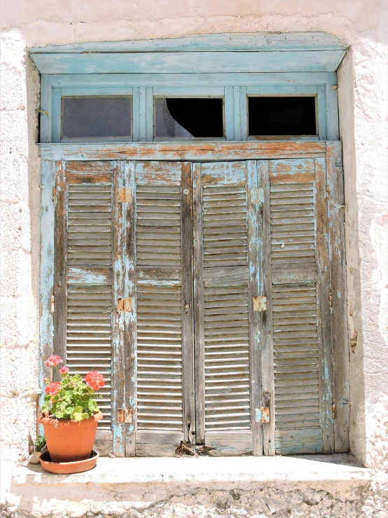 an old wooden door is open above a window with plants in pots