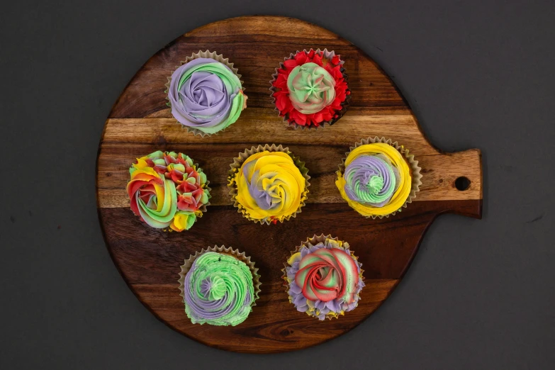 a wooden board topped with cupcakes covered in frosting