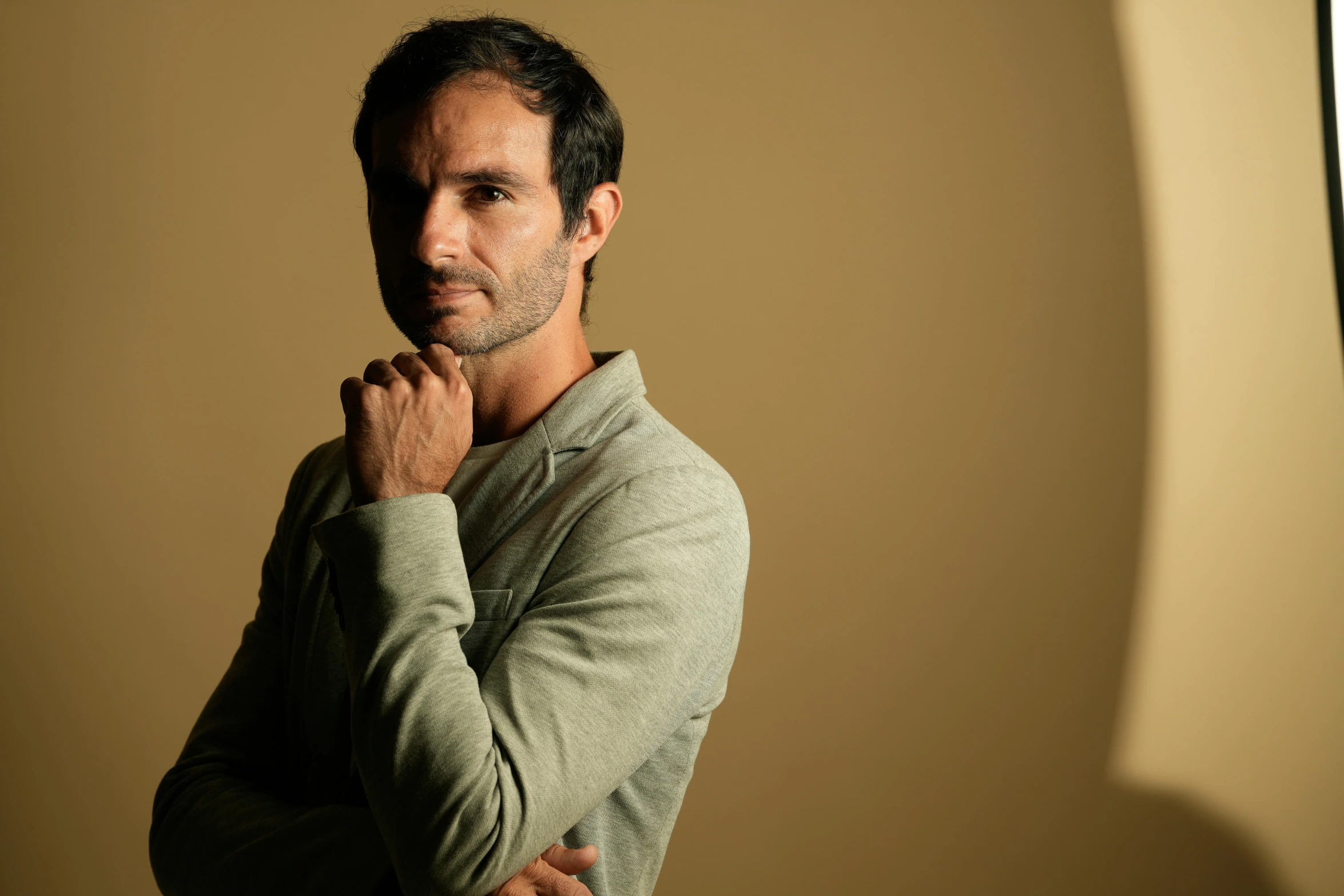 a man standing in front of a beige wall with his hands on his chin