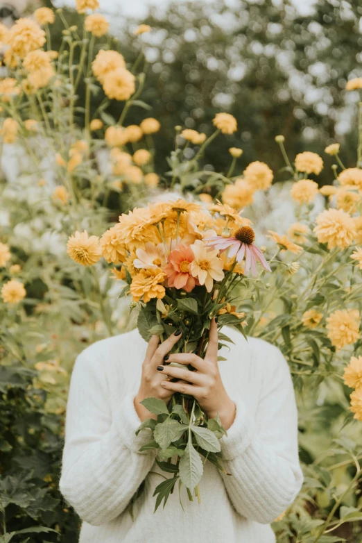 the woman in the field is holding a bunch of flowers