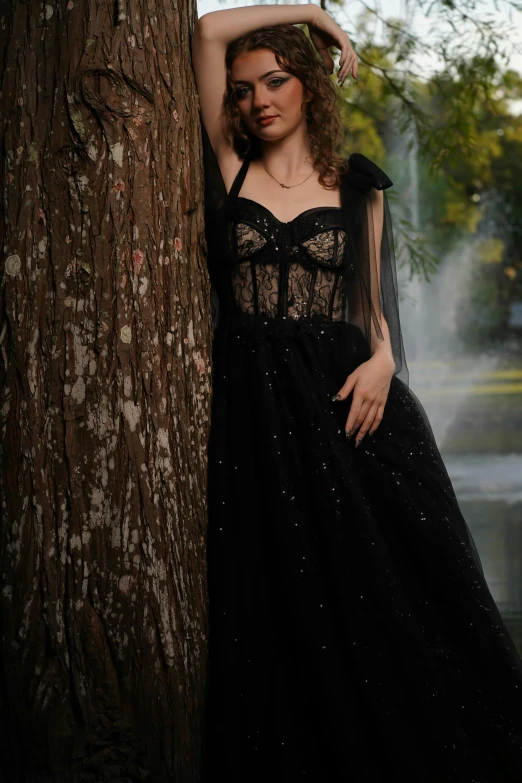 a woman in black dress standing next to a tree