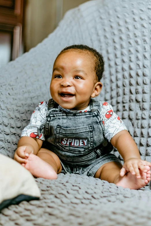 the baby smiles and sits on a couch