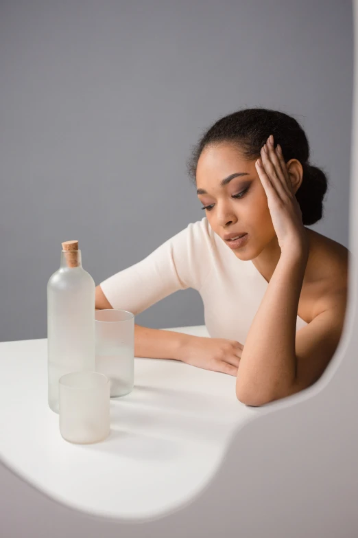 a woman with her hand on the side of her head sitting at a table with a bottle of water