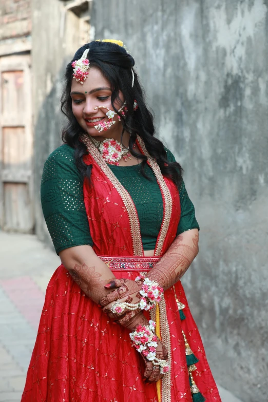 a woman wearing a red and green bridal gown and flowers around her head, smiles